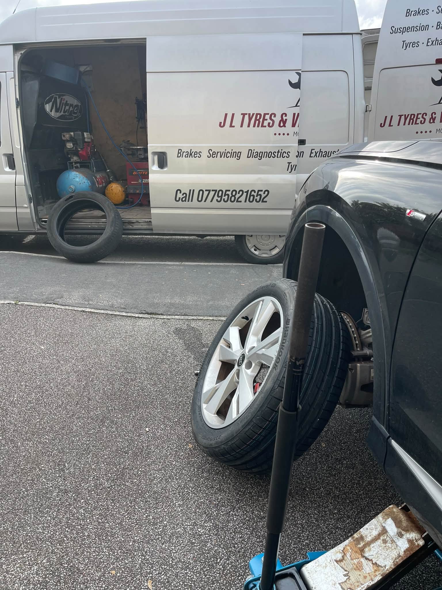 Two J L Tyres vans with a customer's car jacked up and a wheel off on a driveway